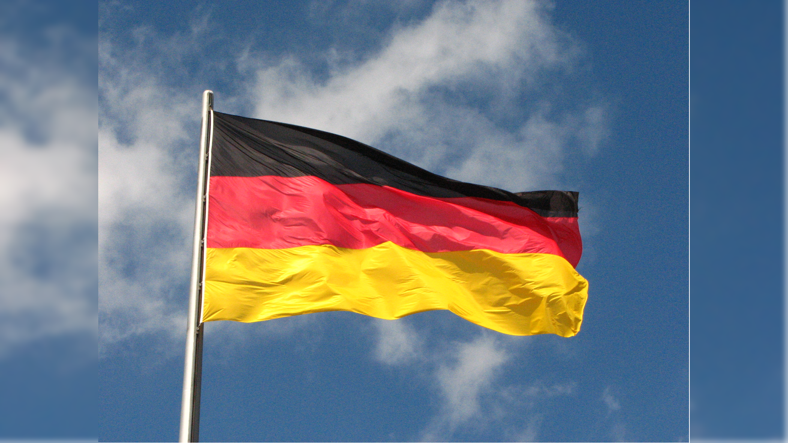 German flag waving against a blue sky, featuring horizontal black, red, and yellow stripes, symbolizing national identity and unity.
