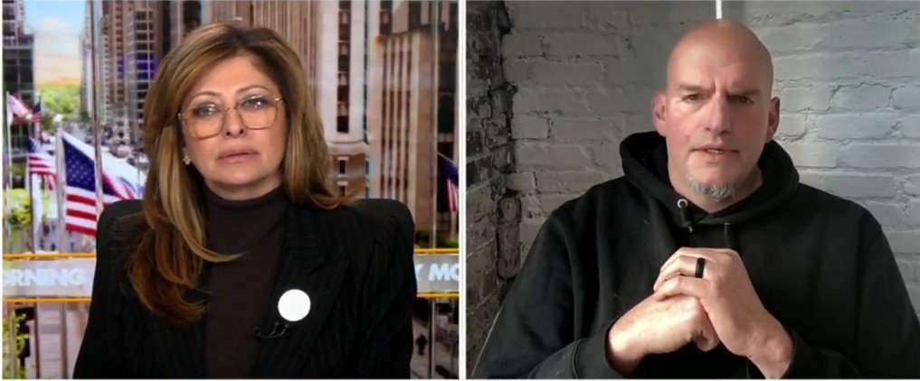 News interview featuring a female host and a male guest discussing current events with a backdrop of cityscapes and flags.
