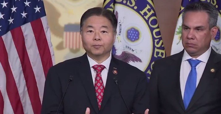 U.S. Congress members giving a press conference, with American flags and official seals in the background, discussing legislative issues.