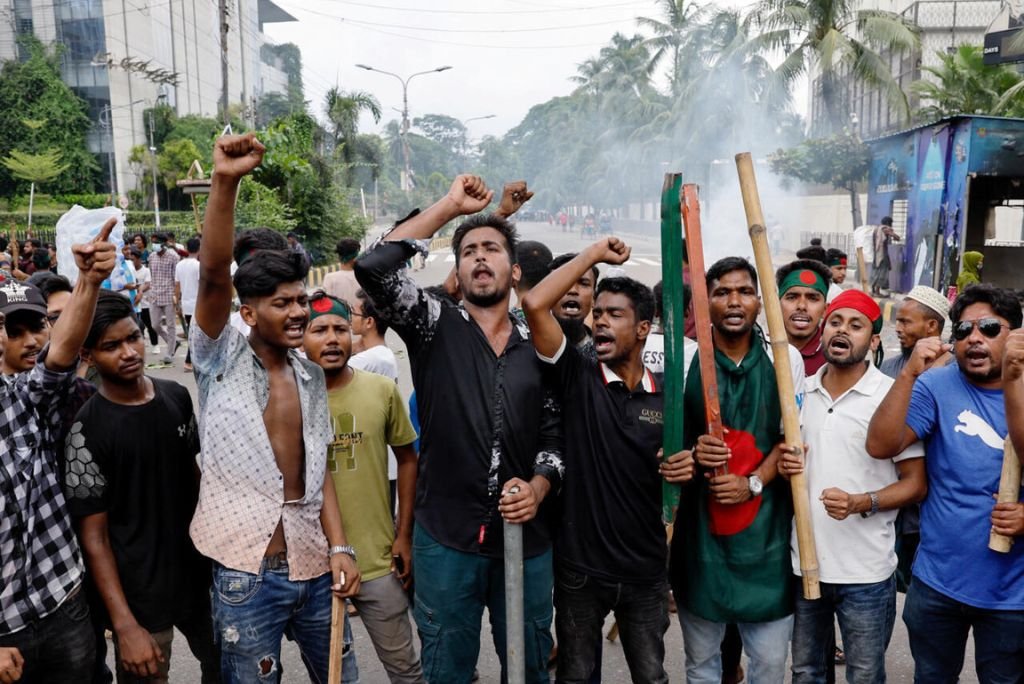 Protesters rallying with raised fists and banners, expressing their demands and solidarity in an urban setting surrounded by palm trees and buildings.