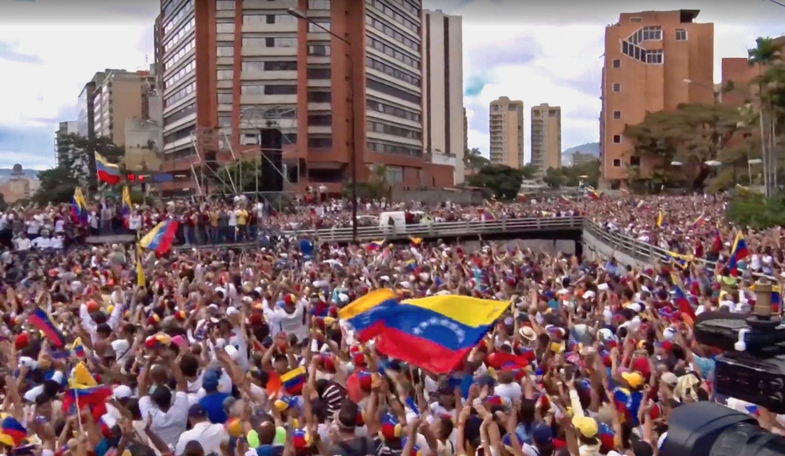 Massive crowd gathered in Venezuela, waving flags and showing support during a political rally in an urban setting.