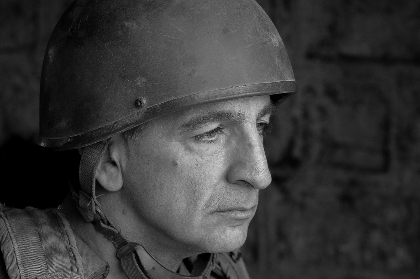 Close-up of a solemn soldier in a military helmet, captured in black and white, reflecting a moment of contemplation.
